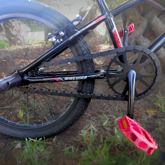 BMX Bikes 16 Inch and larger featuring black chain and red pedals on a Shredder bike in green grass.
