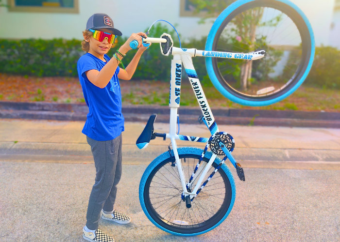 Teenage boy holding a blue and white SE Blocks Flyer bicycle on a street with Blue and white snap-on chain cap for single speed bicycle