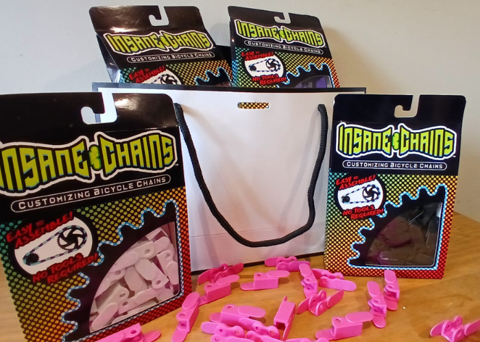Pink, white and black bicycle chain links with 'Insane Chains' packaging on a wooden surface.