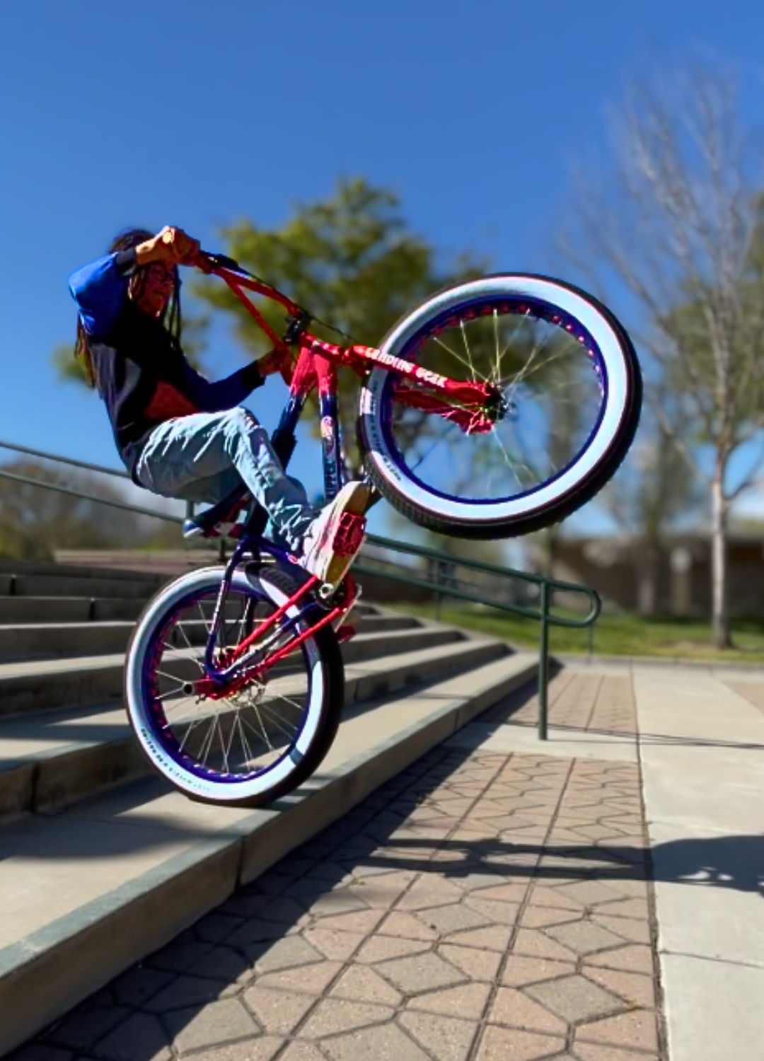 SE PRO Rider Ezra performing a bike trick on a red bicycle with red Insane Chains accessory in an outdoor setting.