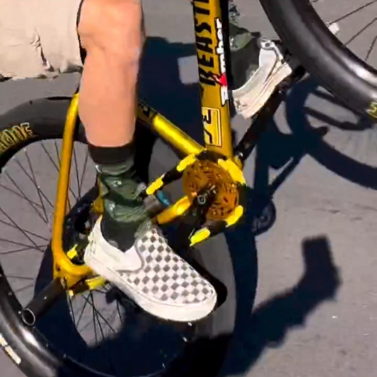 Person riding a Macfox x1s bike with black and yellow accents and checkerboard shoes.