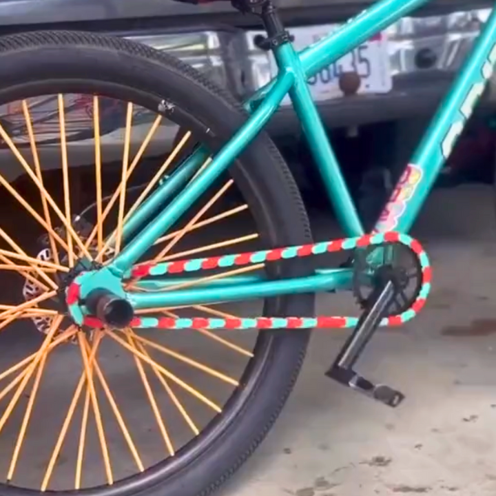 Colored Bike Chain in teal and red tone on a bike with orange spokes in a garage setting.