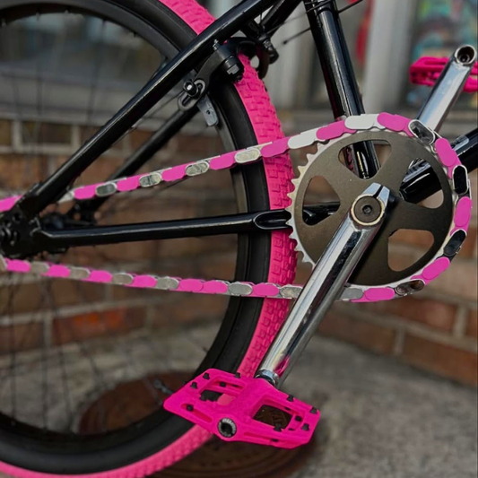 Close-up of a bicycle with pink & chrome Insane Chains, pink peddles and black frame against a blurred background