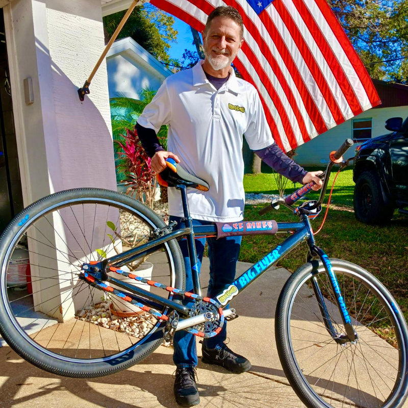 Insane Chains Founder Eric holding a blue SE Big Flyer bicycle showcasing his Insane Chains product in front of an American flag