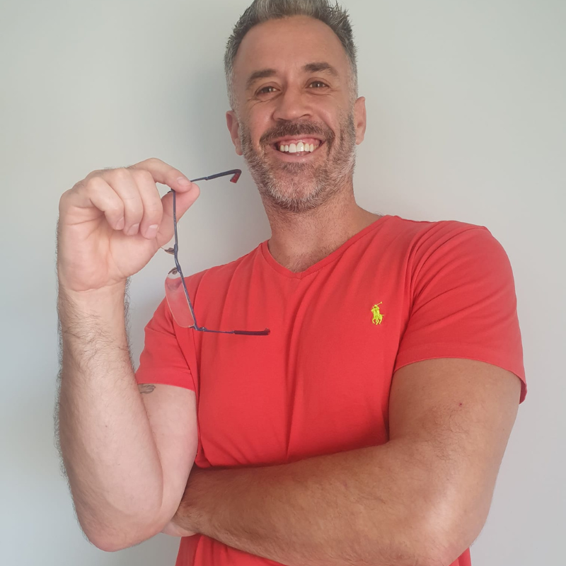 Insane Chains Head of Sales Dan Furlong wearing a red shirt with a logo, holding glasses against a plain background