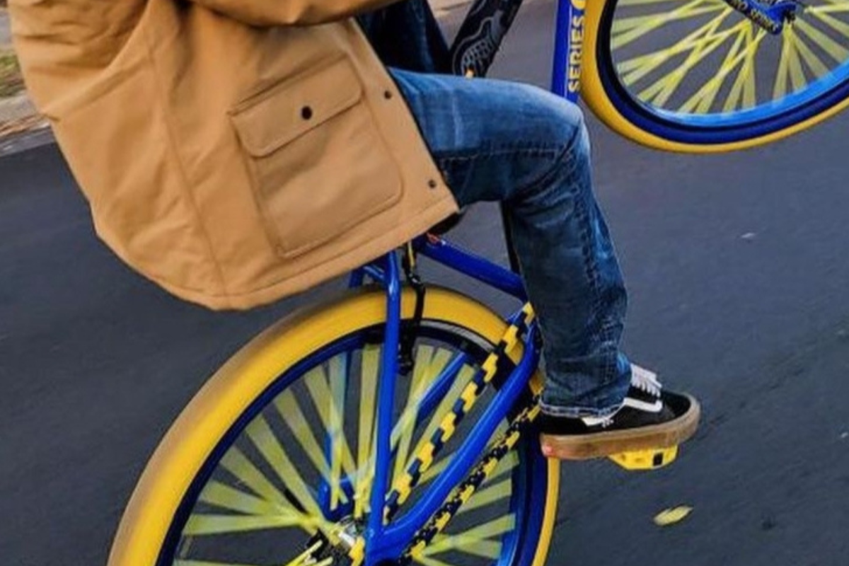Person riding a blue bicycle with yellow and blue chain accessory on a road