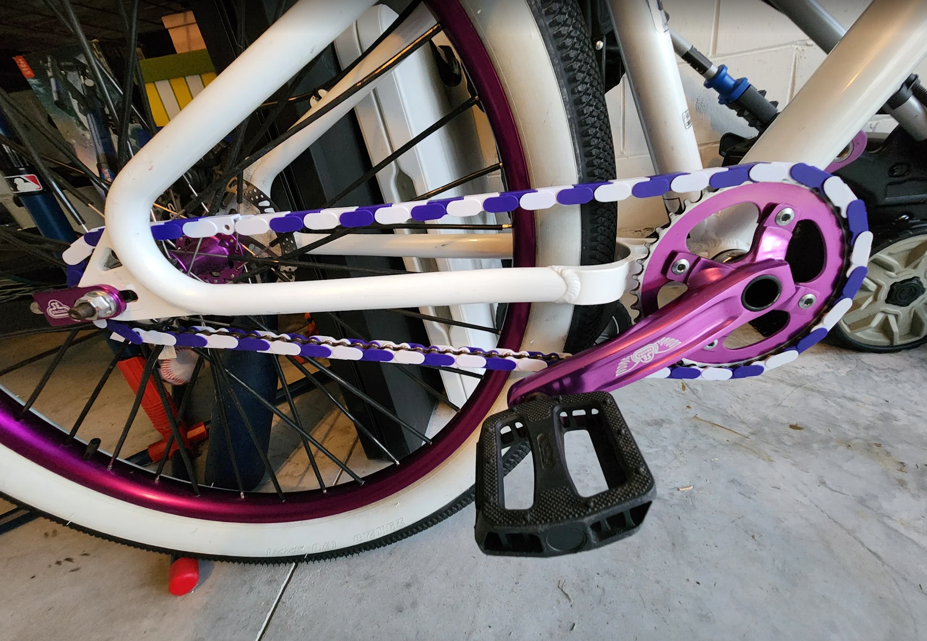Close-up of a bicycle with purple and white chain covers and components on a concrete floor.