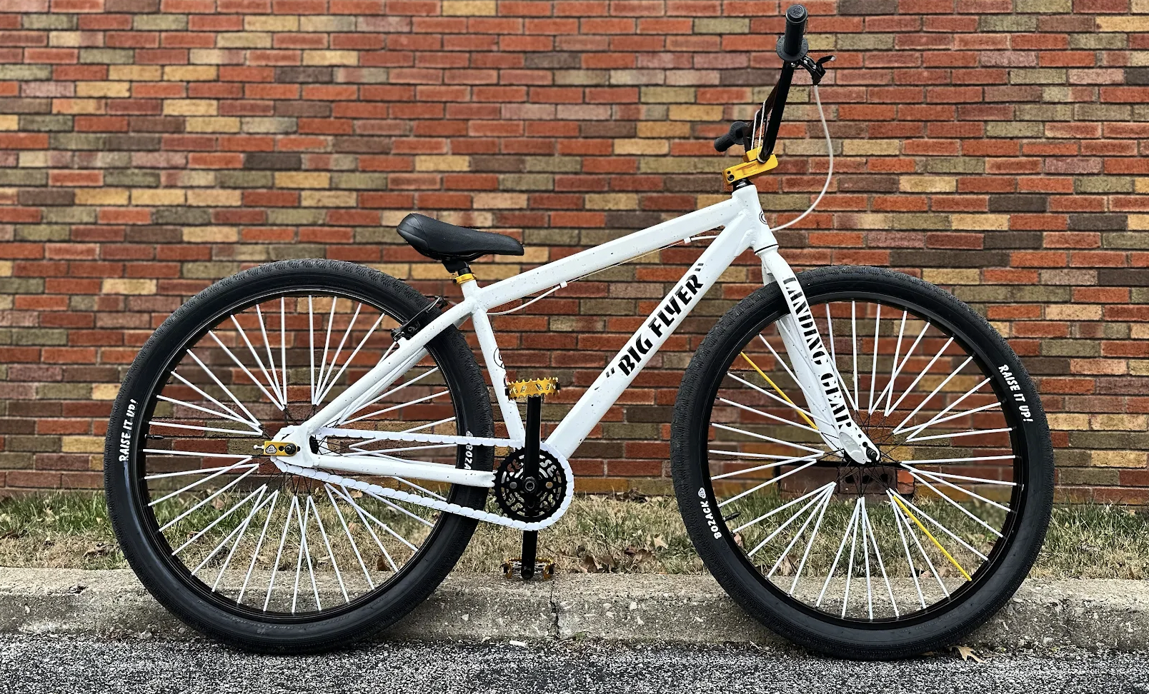 White SE Big Flyer bicycle with white Insane Chain Caps against a brick wall