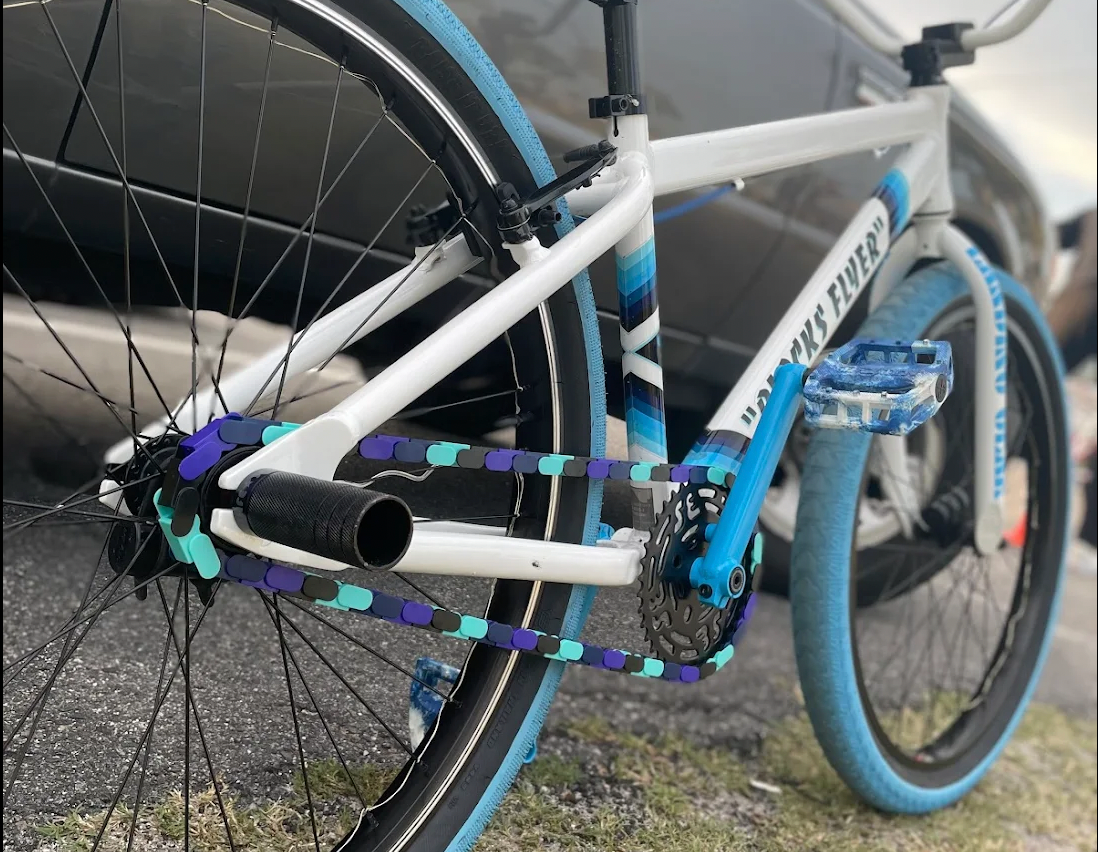 SE Blocks Flyer Bicycle with white & blue frame and tires, with purple teal blue Insane Chain Covers on a road.