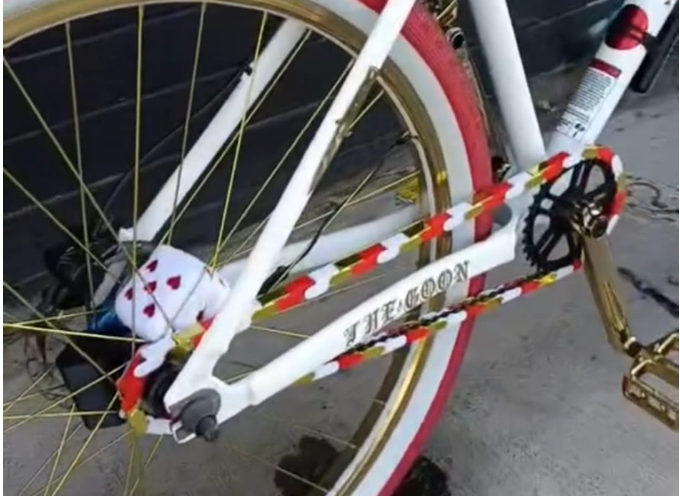 Single Speed Bicycle locked with a red and white and gold chain accessory striped lock on a concrete surface