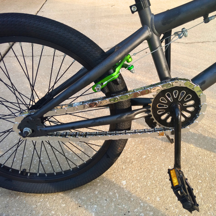 Close-up of insane chain caps snapped onto a black bmx bicycle chain on a concrete surface.