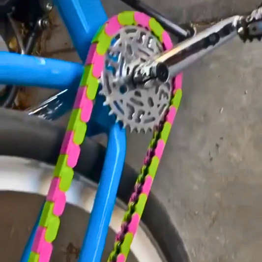 SE Bike Chain in green and pink two tone on a blue bicycle, showcasing its vibrant and stylish design.