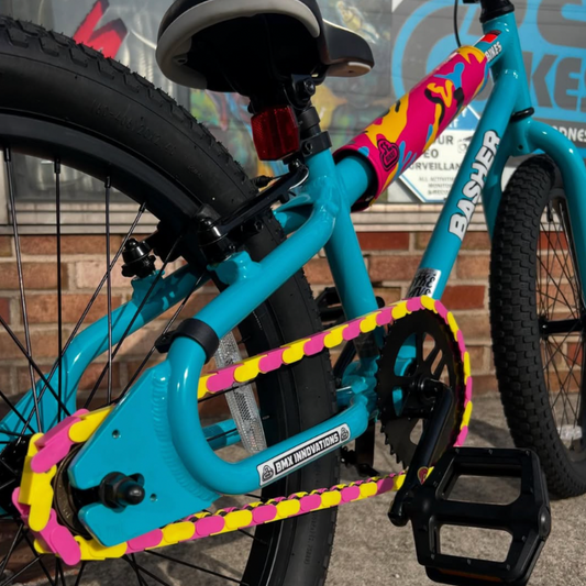 Bike Chain Accessories featuring vibrant pink and yellow two tone snap-on caps on a BMX bike's chain.