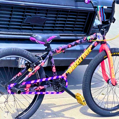 Childrens Bike 14 Inch in purple and pink two tone with bold designs parked near a truck.