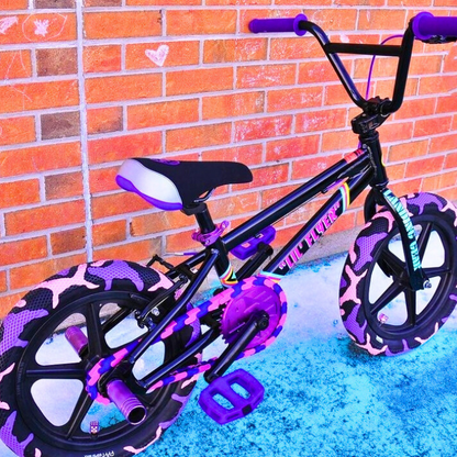 Childrens Bike 14 Inch in purple and pink colors with bold patterned tires against a brick wall background.
