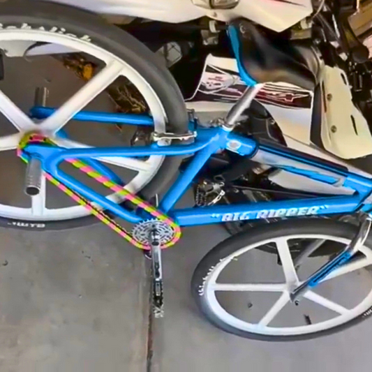 Close-up of an SE Bike Chain in green and pink on a blue bike named "BIG RIPPER" with white wheels.