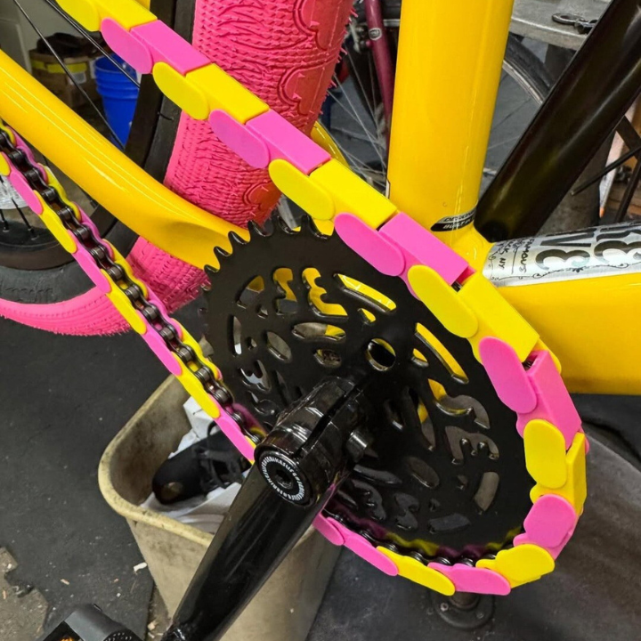Bike Chain Accessories with vibrant pink and yellow two-tone snap-on caps enhancing a bicycle's chain.