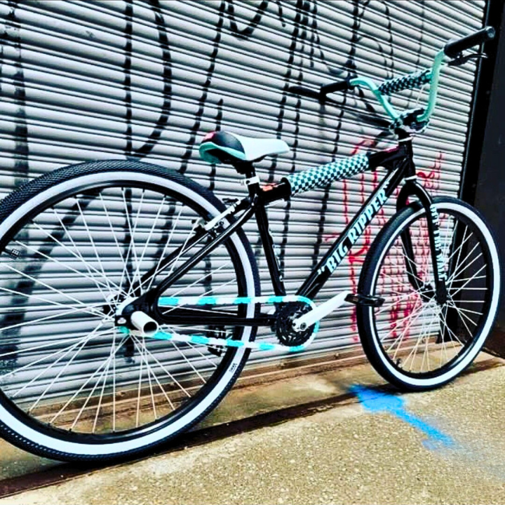 SE Bike Chain on a black and teal BMX bike leaning against a graffiti wall, showcasing a stylish design.