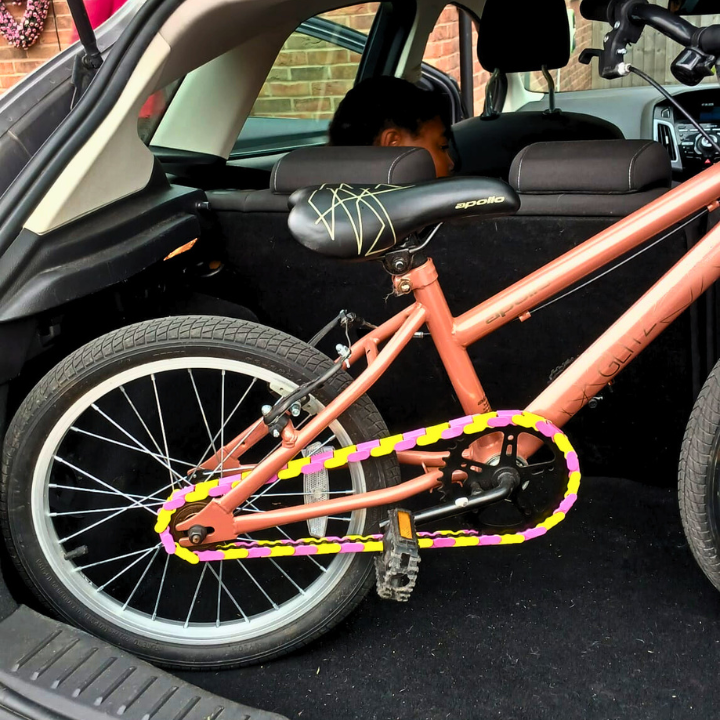 Bike Chain Accessories featuring pink and yellow two tone snap-on caps on a bike in a car trunk.